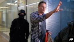 Russian opposition leader Alexei Navalny speaks to the media as a policeman stands guard at the Foundation for Fighting Corruption office in Moscow, Russia, Dec. 26, 2019.