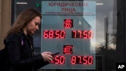 FILE - A woman walks past a currency exchange office display listing the exchange rates of U.S. dollar and euro to Russian rubles, in Moscow, Russia, March 9, 2020. 