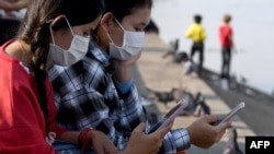 FILE - This photo taken on February 4, 2022, shows students using their smartphones while seated along the riverside in Phnom Penh.