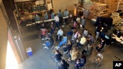 FILE - Migrants released by the Border Patrol with notices to appear in court, Feb. 5, 2022, in Somerton, Ariz., wait for COVID-19 testing at a Regional Center for Border Health warehouse.