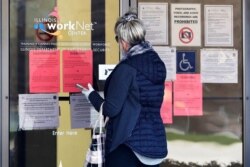 FILE - A woman checks job application information in front of IDES(Illinois Department of Employment Security)/WorkNet center in Arlington Heights, Ill., April 9, 2020.
