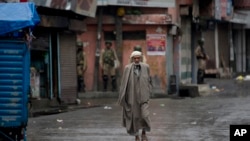 Seorang pria Kashmir berjalan di tengah jalanan yang sepi, di Srinagar, kawasan Kashmir yang dikuasai oleh India, diawasi oleh para penjaga keamanan, 14 Agustus 2019. 