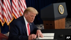 President Donald Trump signs one of four executive orders addressing the economic fallout from the COVID-19 pandemic at his Trump National Golf Club in Bedminster, N.J., Saturday, Aug. 8, 2020. Trump signed the executive orders and bypassed the…