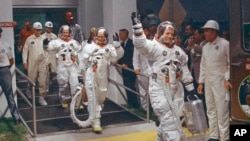 FILE - Neil Armstrong waving in front, heads for the van that will take the crew to the rocket for launch to the moon at Kennedy Space Center in Merritt Island, Florida, July 16, 1969.