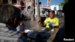 FILE - Men play cards in Mariachi Plaza in the Boyle Heights area of Los Angeles, home to many Mexican and Central American migrants.