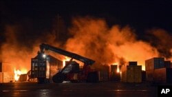 Api muncul dari kontainer yang terbakar di lokasi serangan rudal, di pelabuhan kota pesisir Latakia, Suriah, Selasa, 28 Desember 2021. (Foto: SANA via AP)