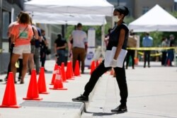 FILE - A medical assistant, right, provides paperwork to people in line at a walk-up COVID-19 testing site in Dallas, Texas, June 11, 2020.