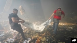 دو نفر در ممیان خرابه‌های به جا مانده از حملات موشکی روسیه آن چه را یافته‌اند با خود حمل می‌کنند